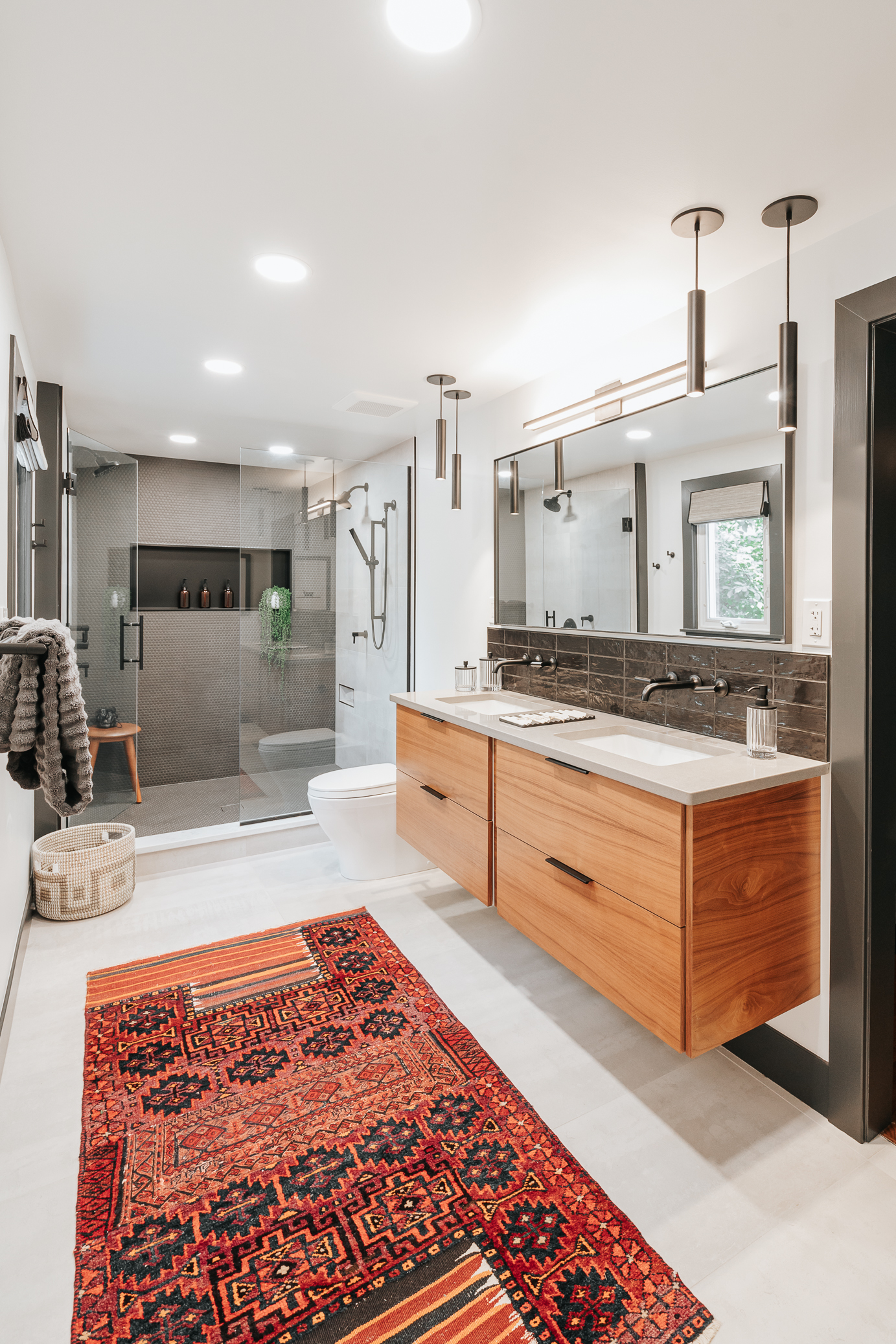 Modern spa-like bathroom in West Bloomfield featuring a floating wood vanity with double sinks, frameless glass shower, and a vibrant patterned rug.