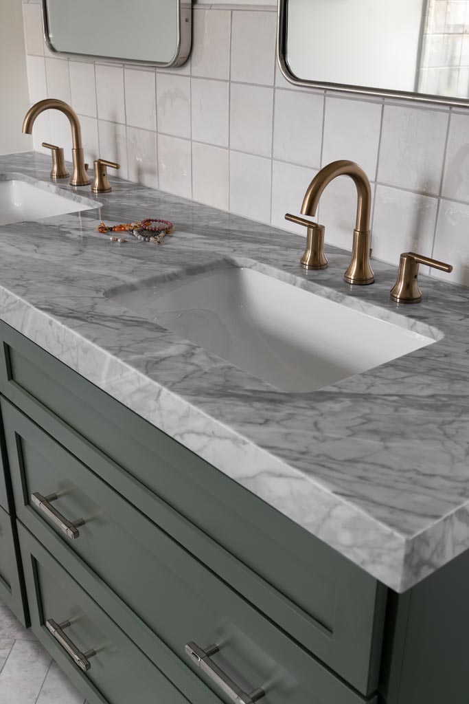 Close-up of marble bathroom countertop with gold fixtures and green cabinetry in an Ann Arbor, MI home remodel.