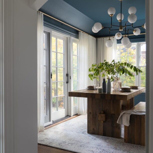 Elegant dining room with wooden table, bench seating, and plants framed by a white archway in a luxury Ann Arbor, MI renovation.