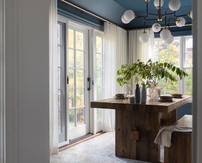 Elegant dining room with wooden table, bench seating, and plants framed by a white archway in a luxury Ann Arbor, MI renovation.