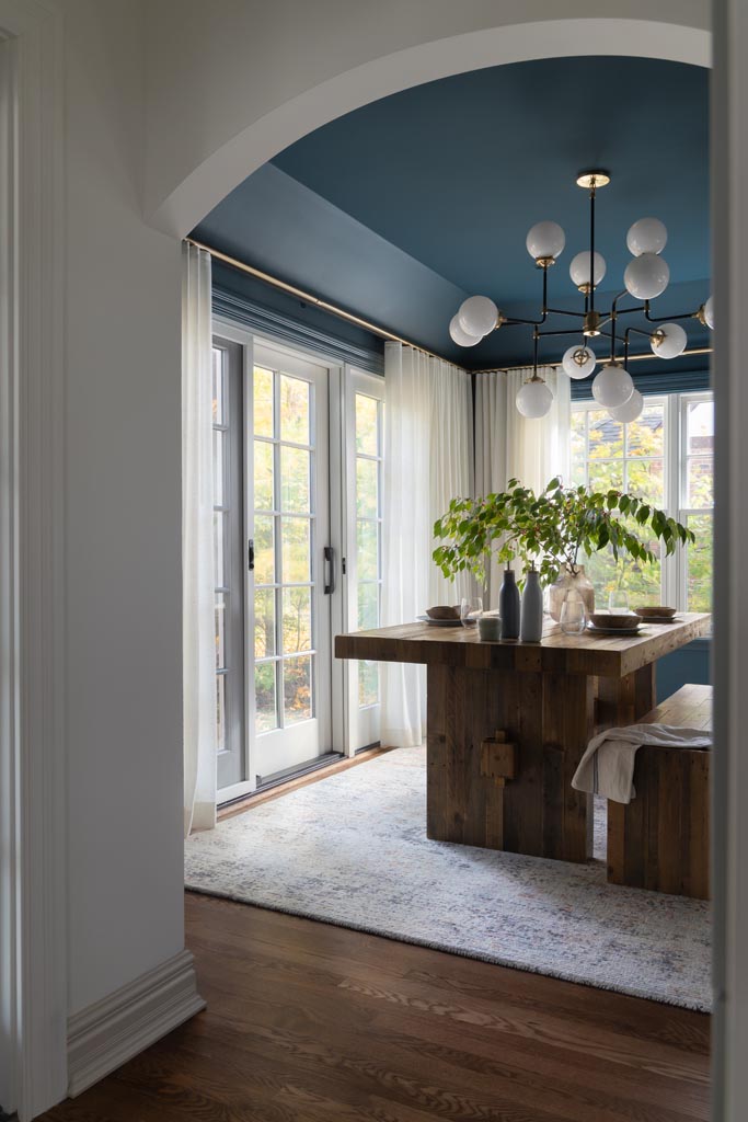 Elegant dining room with wooden table, bench seating, and plants framed by a white archway in a luxury Ann Arbor, MI renovation.