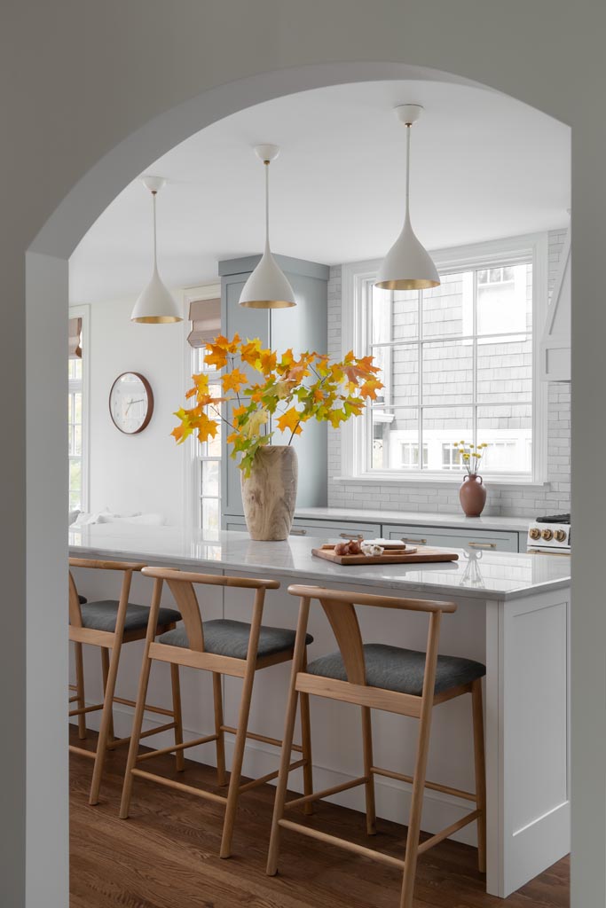 Bright modern kitchen featuring natural stone countertops, wooden barstools, pendant lighting, and soft gray cabinetry in Ann Arbor, MI.