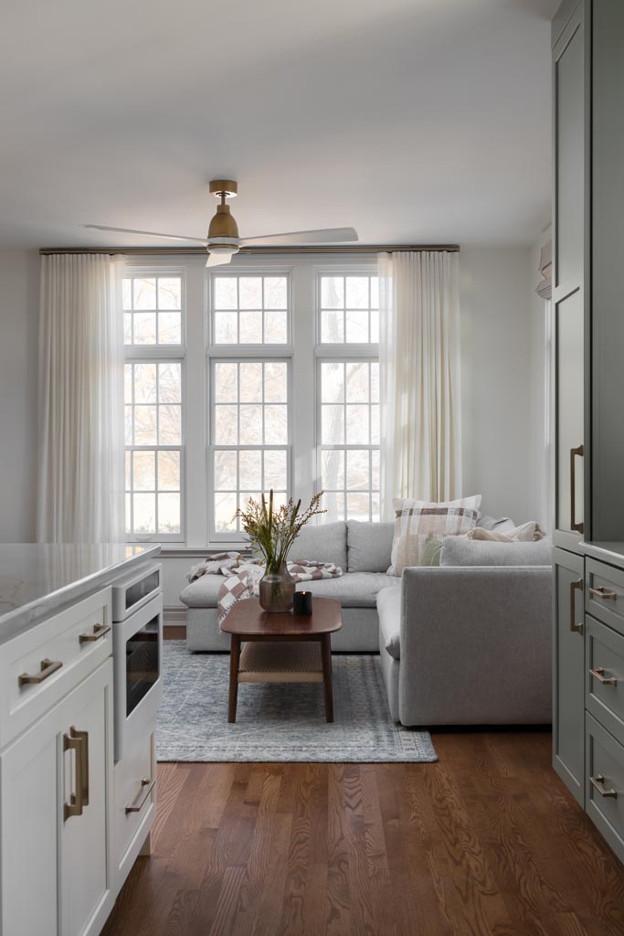 Spacious living room with gray sectional, large windows, and greenery in an Ann Arbor, MI luxury home renovation.