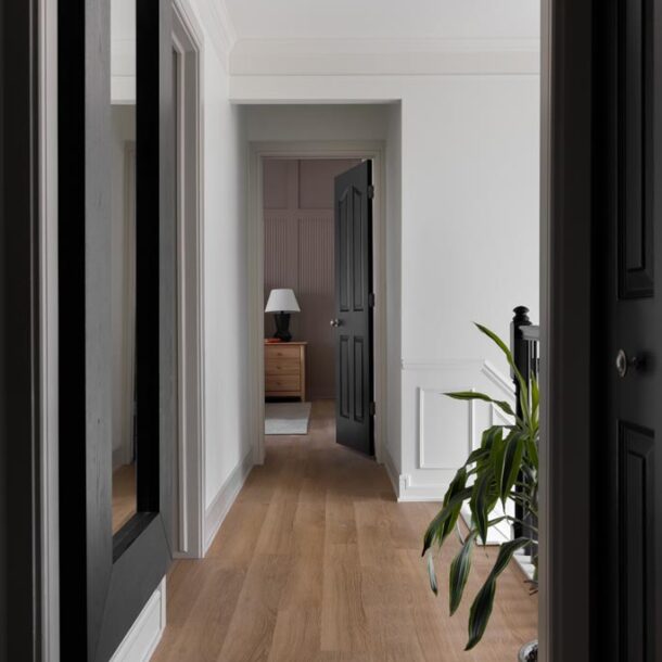Bright hallway with natural wood floors, white walls, and black doors leading to a bedroom in a Canton, MI renovation.