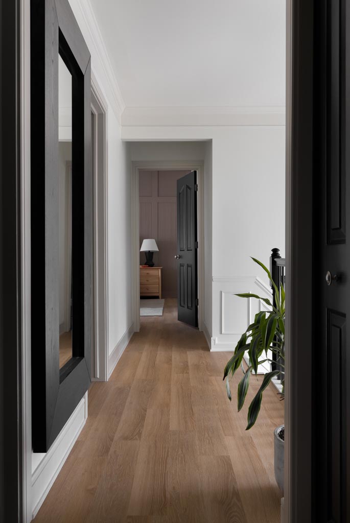 Bright hallway with natural wood floors, white walls, and black doors leading to a bedroom in a Canton, MI renovation.
