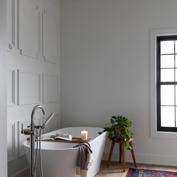 Luxurious white freestanding bathtub with panel accent wall, large window, and red patterned rug in a renovated Canton, MI bathroom.