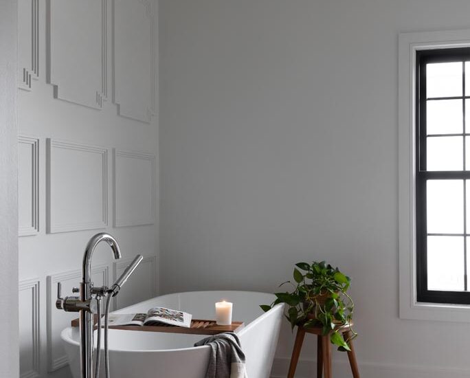 Luxurious white freestanding bathtub with panel accent wall, large window, and red patterned rug in a renovated Canton, MI bathroom.
