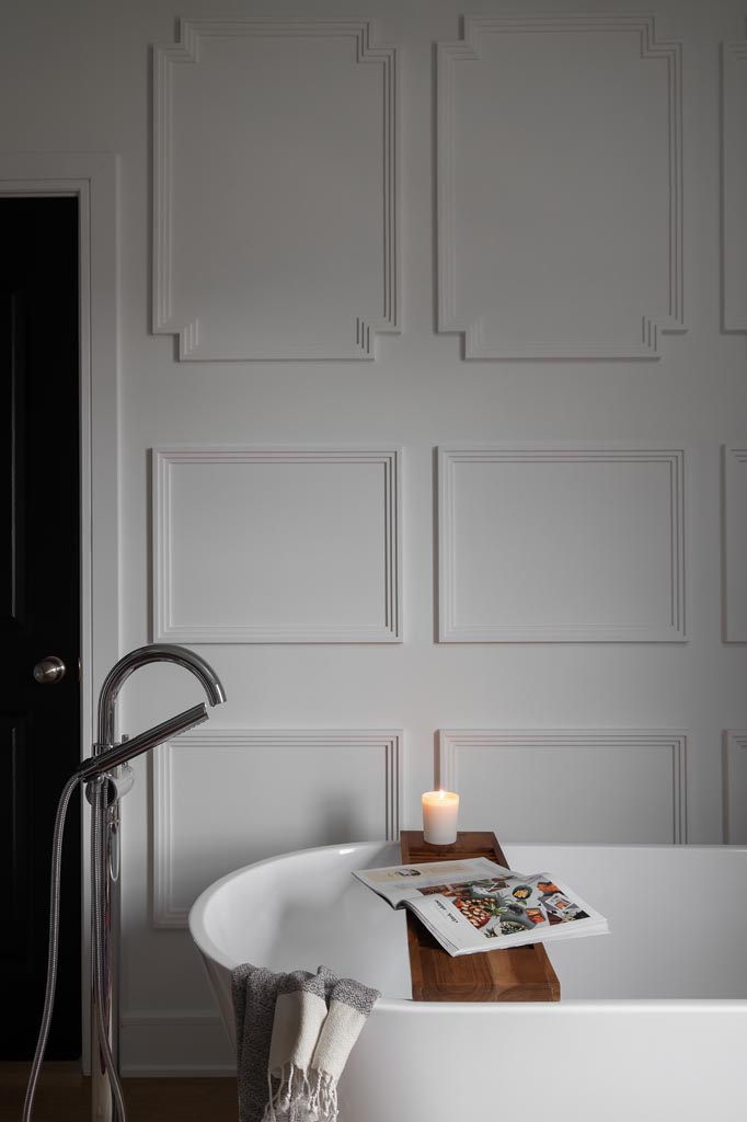 White bathtub against decorative wall paneling, soft candlelight, and detailed interior design.