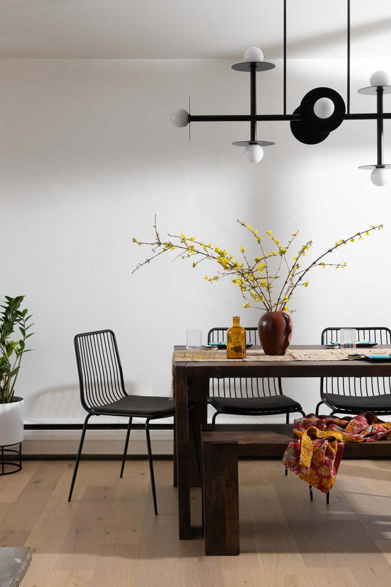 Modern dining room in Royal Oak, MI, with a wooden table, black chairs, and a centerpiece featuring yellow blossoms.