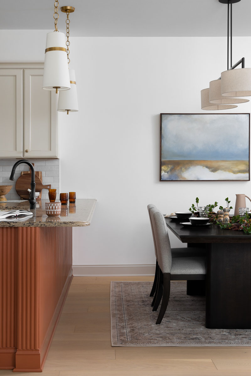 Elegant dining area in Ann Arbor, MI, featuring a custom dark wood table, upholstered chairs, modern lighting, and a view of a luxury kitchen with custom cabinetry and stone countertops.
