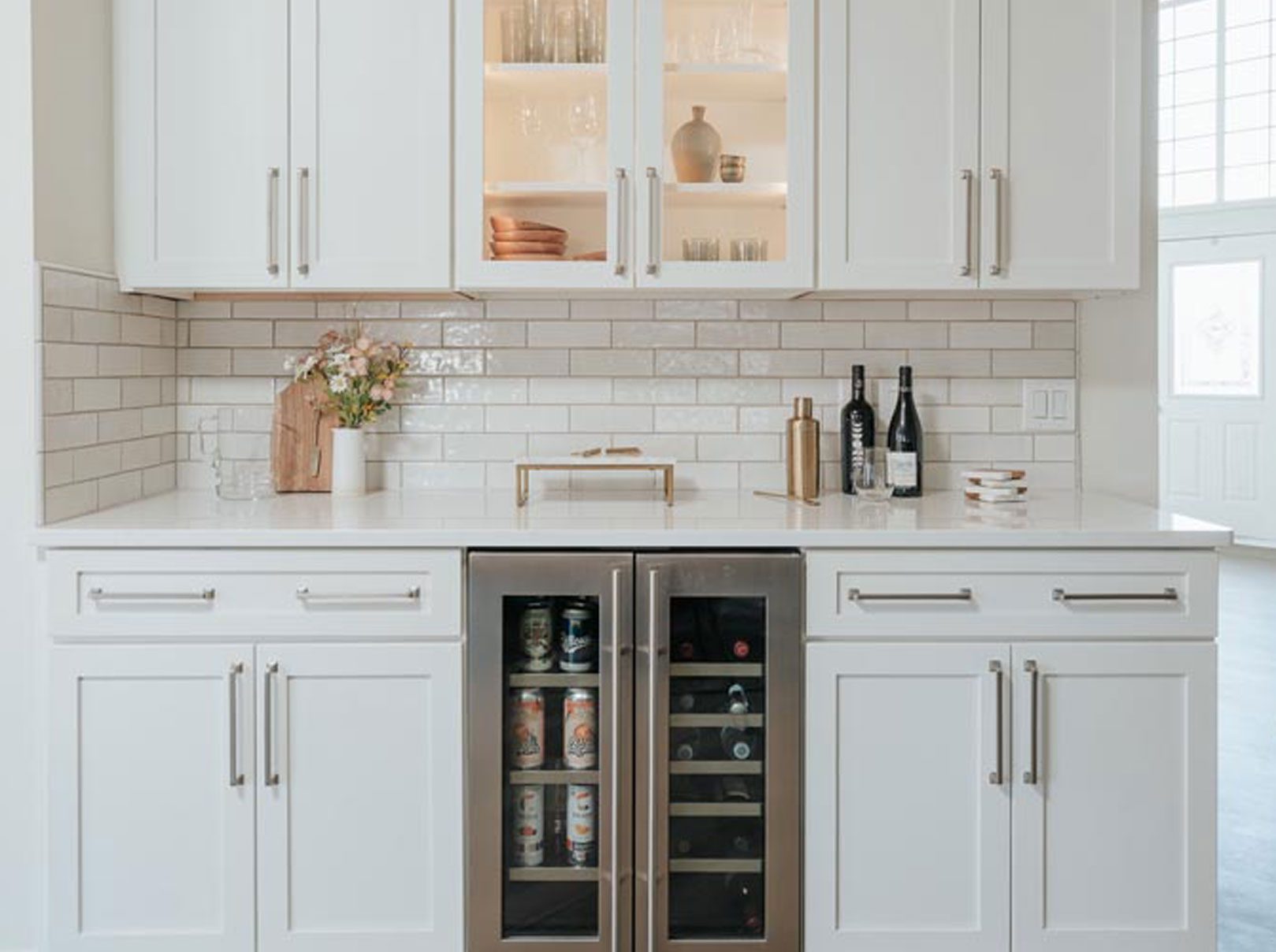 Luxury beverage station featuring white cabinetry, glass display shelves, a stainless steel wine cooler, and a white subway tile backsplash Novi, Michigan.