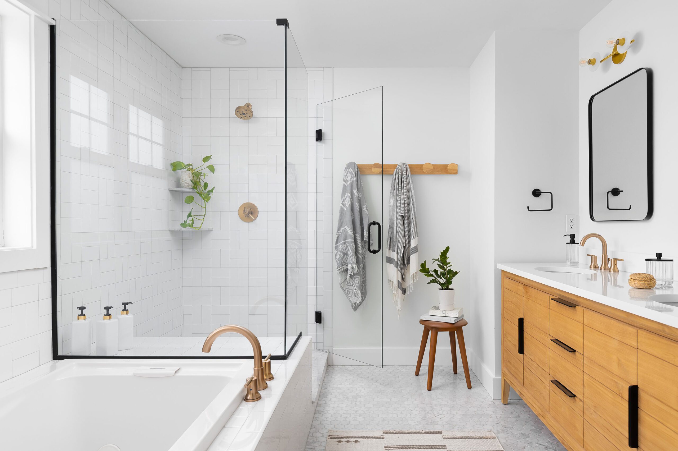 A spa-like bathroom in Royal Oak, Michigan, featuring a light and airy design with brass fixtures, white oak cabinetry, a walk-in shower with black-framed glass, and greenery accents.