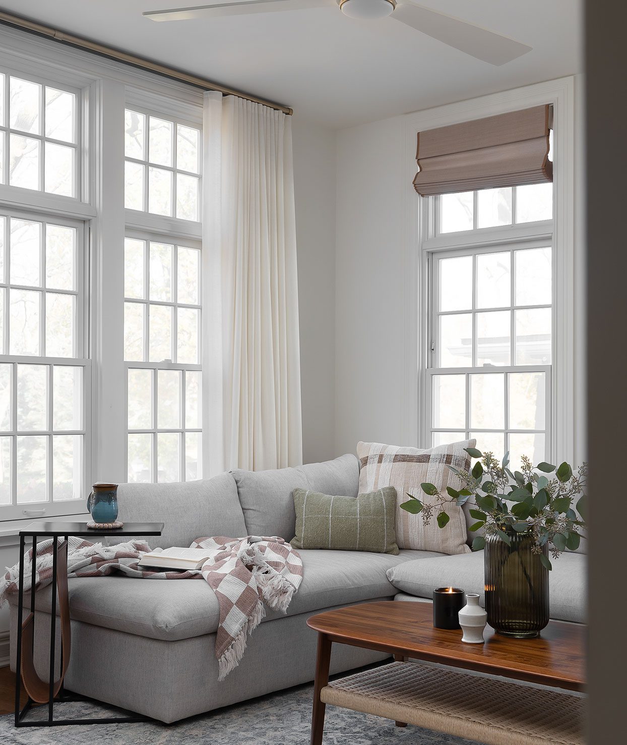 Construction and remodeling by Clark + Aldine – a biophilic living room with natural light, featuring a gray sectional, wood coffee table, indoor plants, and nature-inspired decor in neutral tones, ready for move-in.