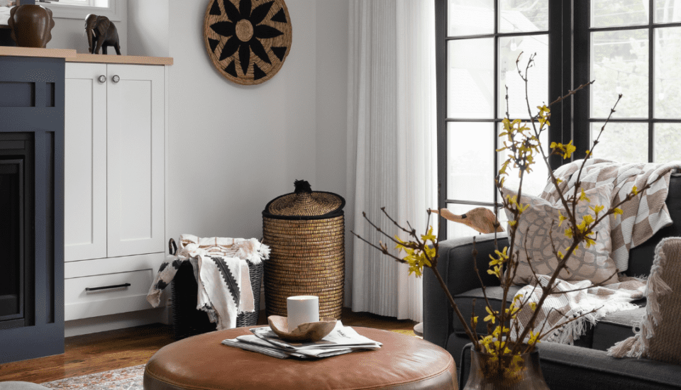 A warm, inviting living room with natural textures and cozy seating, perfect for November family gatherings. Features a leather ottoman, patterned area rug, and nature-inspired decor.