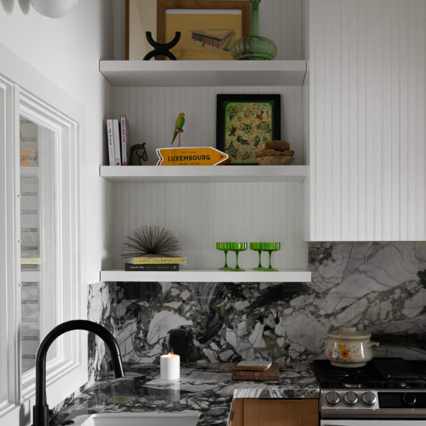 A luxurious modern kitchen with striking marble countertops and backsplash, open shelving with eclectic decor, and a matte black faucet. This kitchen design combines high-end materials with unique decorative accents, creating a visually captivating space. Perfect for homeowners seeking inspiration to elevate their modern luxury kitchen design.