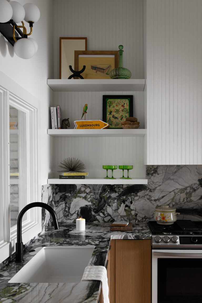 A luxurious modern kitchen with striking marble countertops and backsplash, open shelving with eclectic decor, and a matte black faucet. This kitchen design combines high-end materials with unique decorative accents, creating a visually captivating space. Perfect for homeowners seeking inspiration to elevate their modern luxury kitchen design.