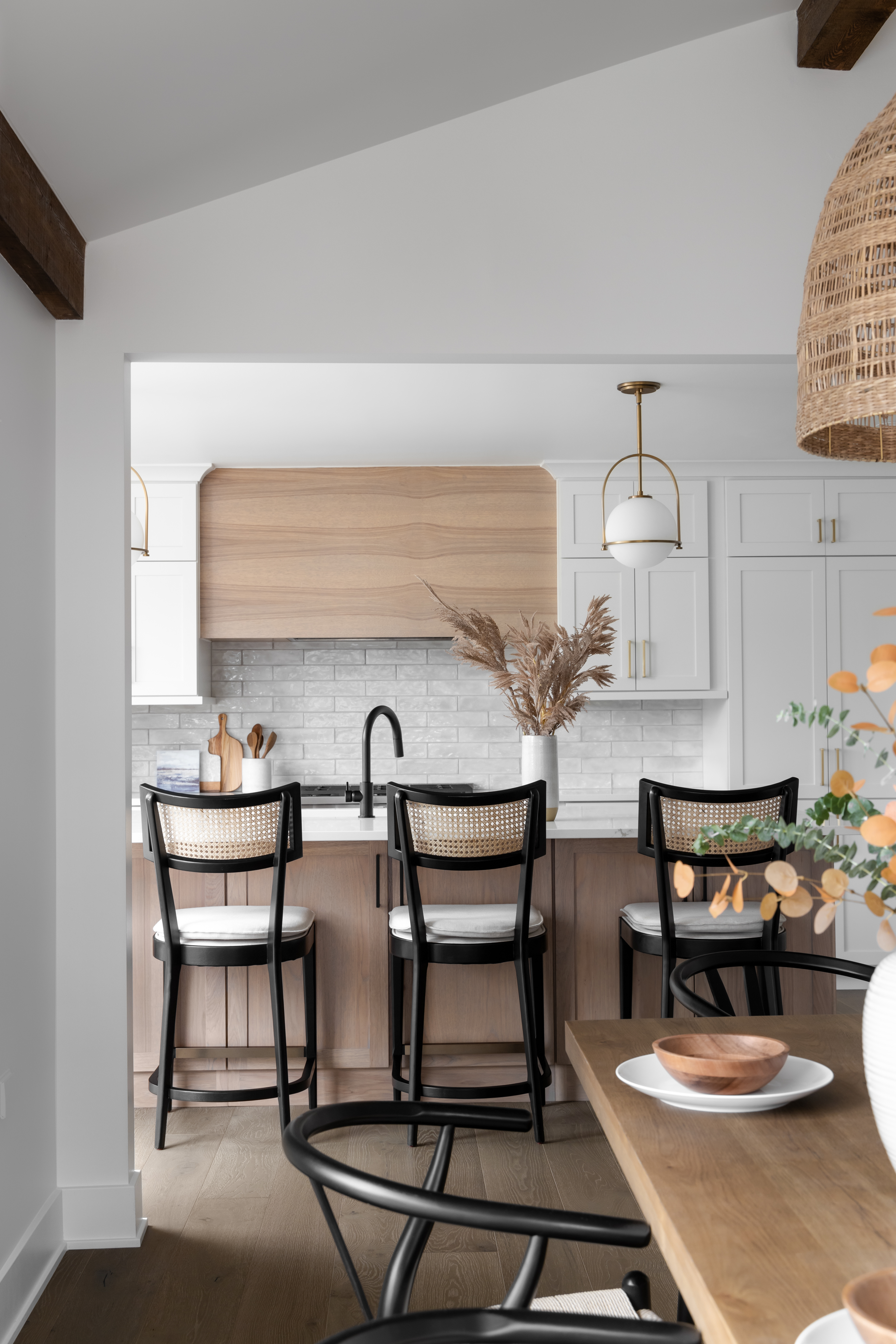 Open-concept luxury kitchen featuring natural wood accents, white cabinetry, black barstools with cane backing, and modern pendant lighting in Plymouth, Michigan.