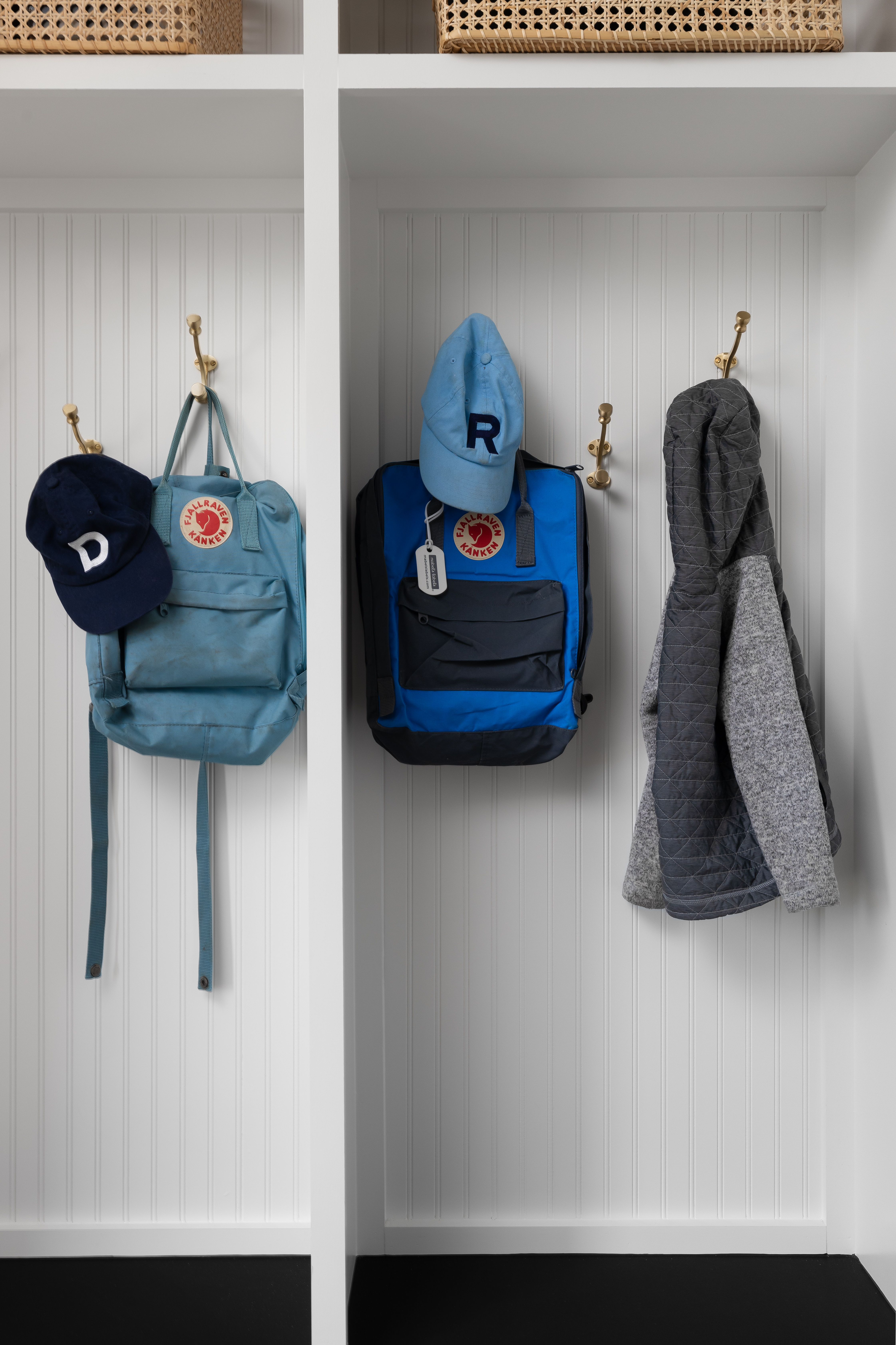 Mudroom storage with individual cubbies for kids, featuring hooks for backpacks, hats, and coats, as well as woven baskets on the top shelf for extra storage.