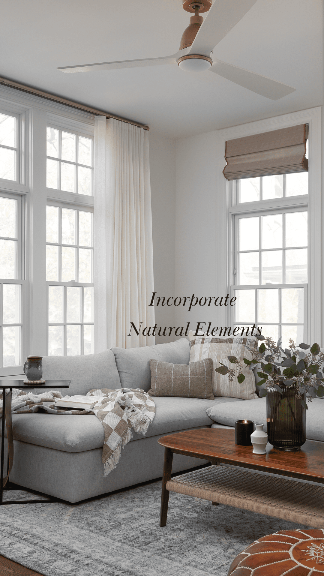 A cozy living room with a gray sectional, wood coffee table, and greenery. The space highlights biophilic design with natural elements and soft textures for a relaxing environment.