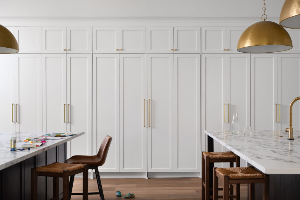 Modern luxury kitchen featuring sleek white cabinetry with brass handles, marble countertops, and statement pendant lighting.